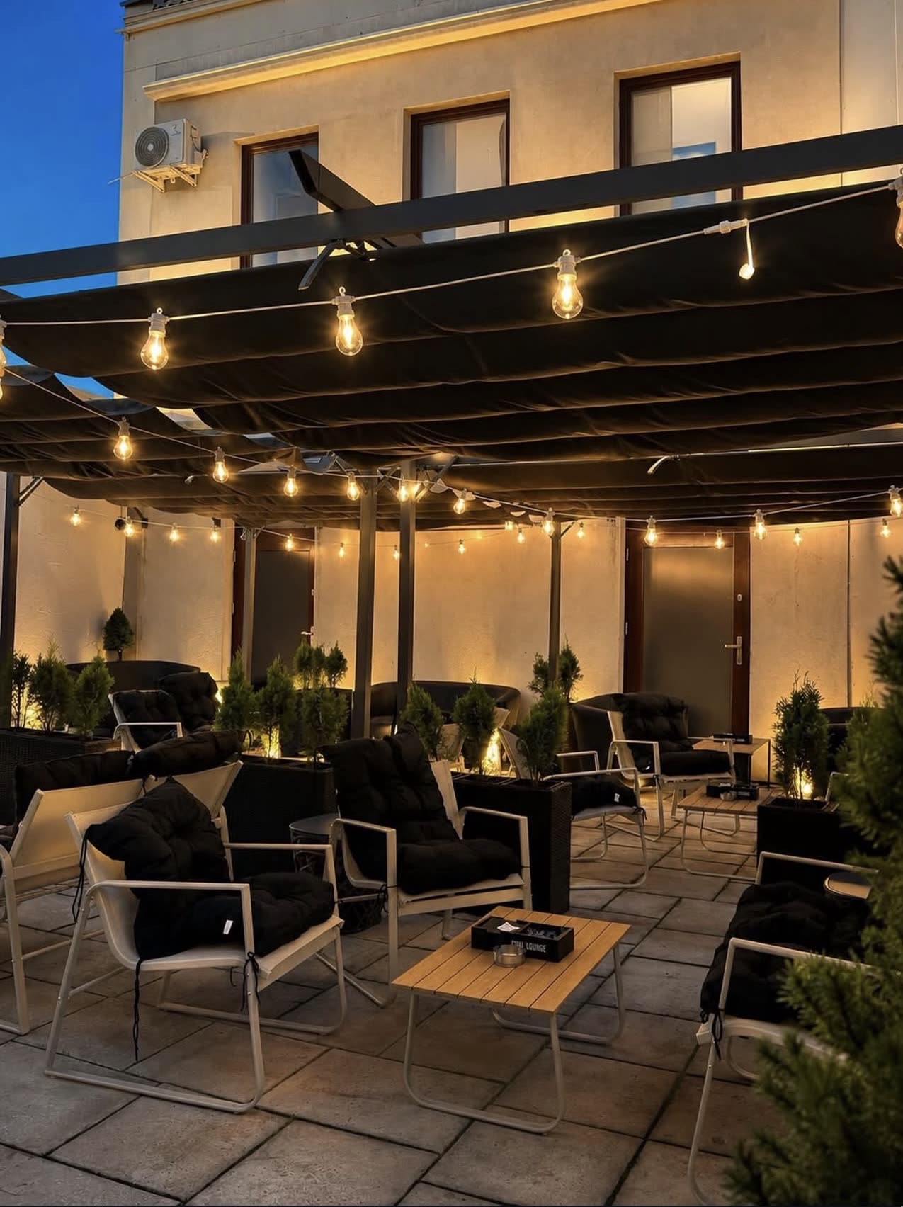 Letni ogródek Chill Lounge wieczorem - pergola ze sznurami żarówek