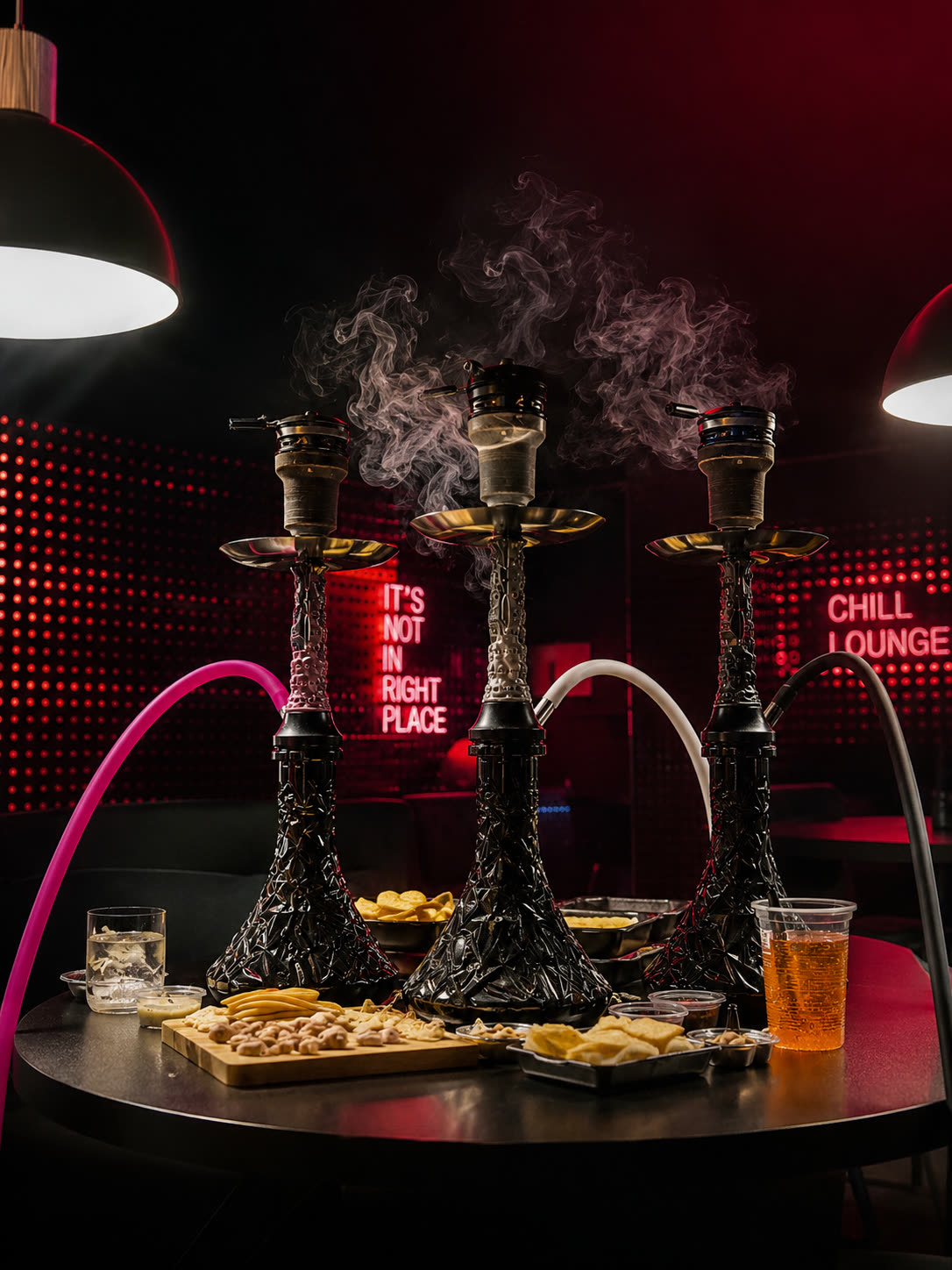 Trzy shishy z dymem na stole pod czerwonym neonem Chill Lounge